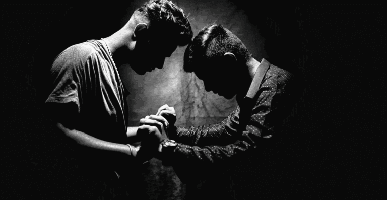 Dois homens um de frente para o outro de mãos dadas orando.