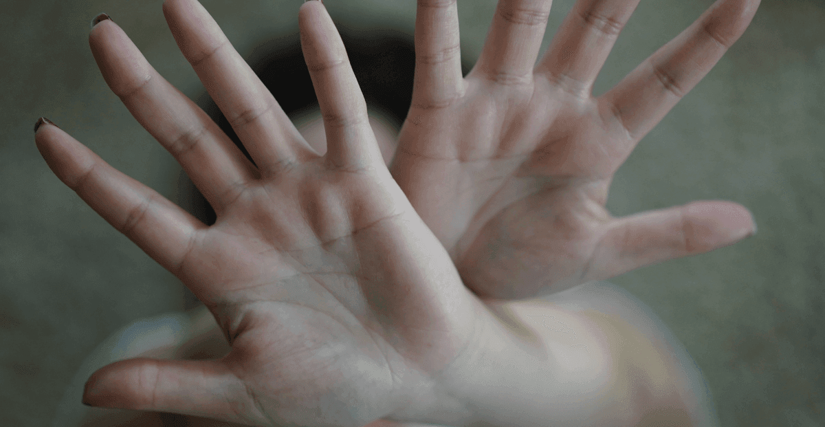 Uma mulher com as duas mãos abertas a frente do rosto, com se estivesse se escondendo de algo.