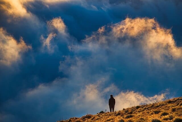 Um homem sozinho no alto de um monte olhando para um lindo céu azul